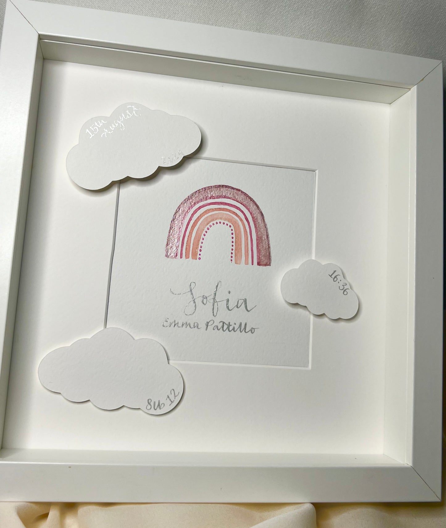 Angled painting of rainbow showing metallics in watercolours. Framed baby painting, personalised with details and clouds.