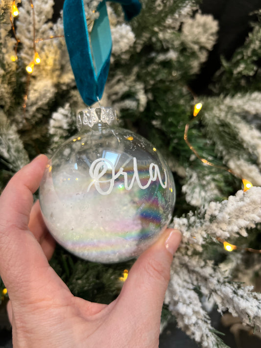 Glass Christmas Bauble personalised with Orla in hand written calligraphy against a tree