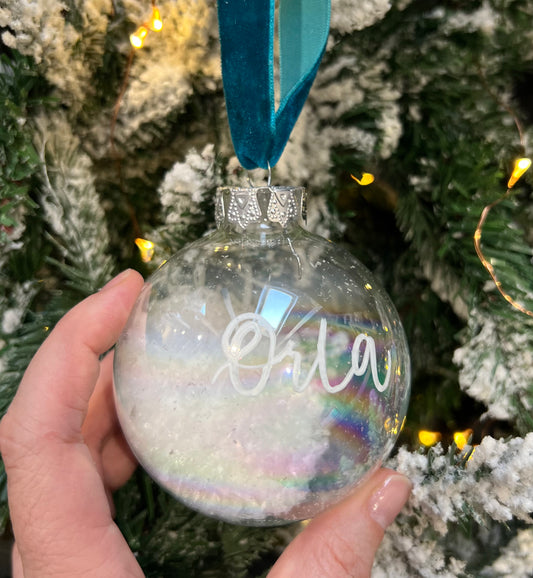 Glass Bauble with snow and Orla in handwritten calligraphy against a christmas tree