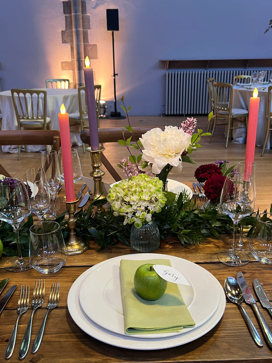 Beautiful table setting, picnic style wedding. Green apple with leaf, white card place card leaf with black ink calligraphy guest name. Summer wedding place card. On rustic wooden table. Apple, pear, orange.