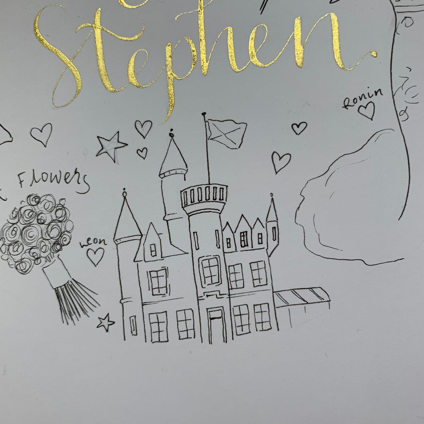 Close up image of Hand drawn bespoke wedding doodle card personalised with wedding features such as the drawing of Carlowire Castle with the Bride and grooms first names handwritten in gold ink calligraphy above.