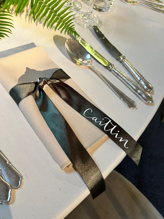 Personalised green ribbon with white name, tied around napkin from 88 events, on beautifully set table with ferns