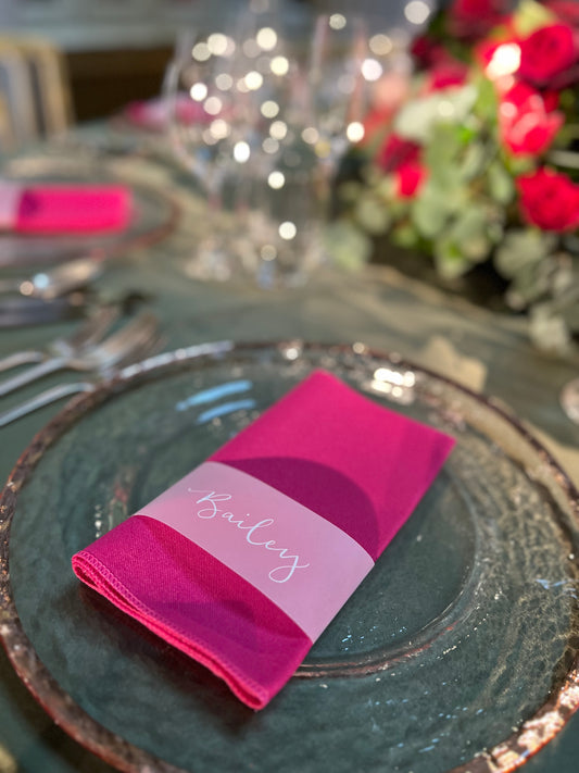 vellum band going around pink napkin sitting on rose gold charger plate. white ink calligraphy on vellum band with guest name