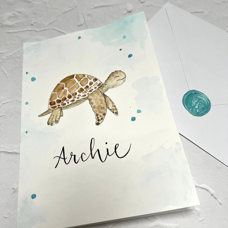 hand painted card with swimming turtle on front and handwritten name archie on front. envelope in background with blue baby wax seal 