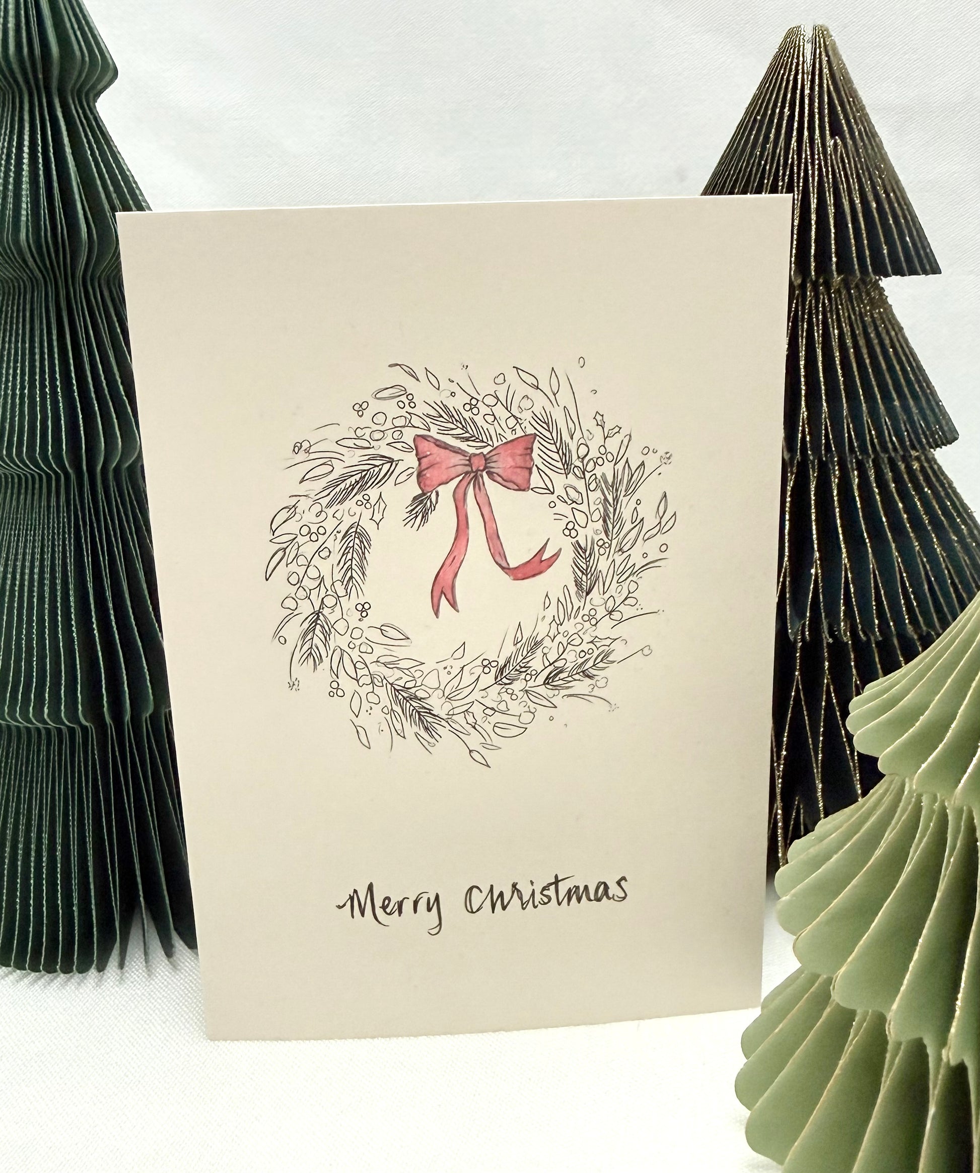 Christmas card with wreath and bow design, surrounded by decorative trees on a white background
