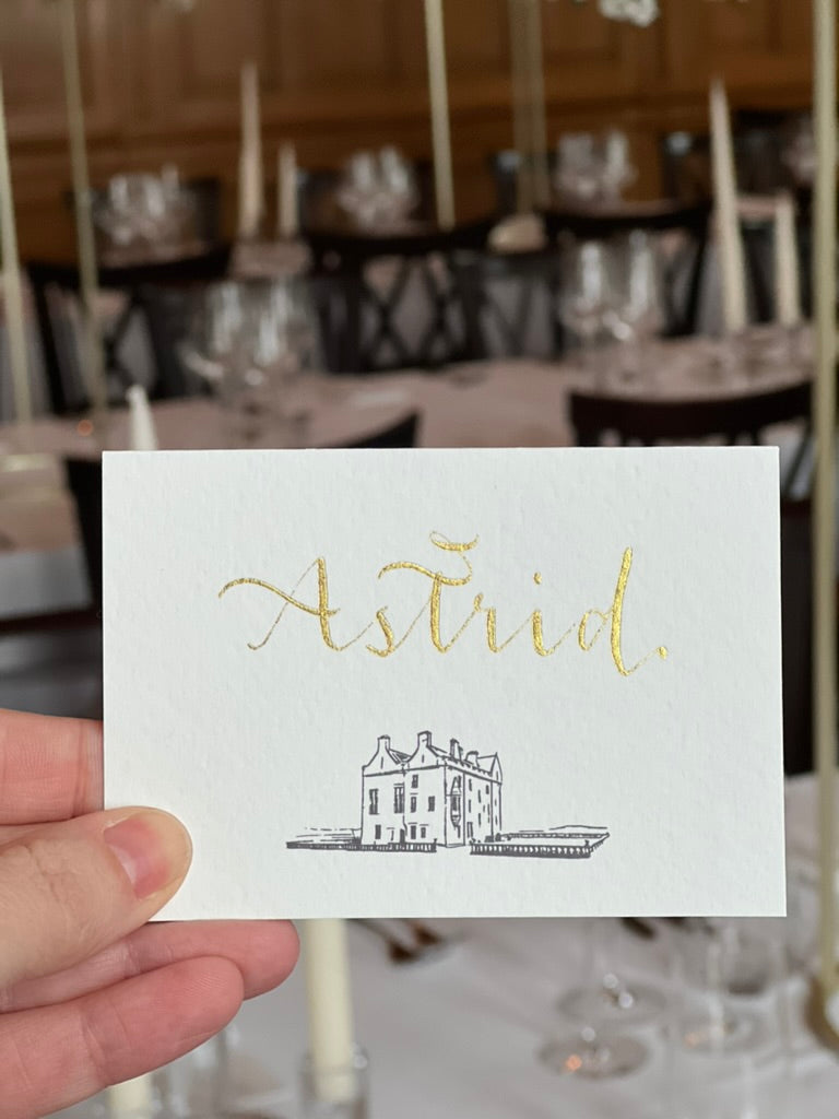 Beautiful wedding and event place cards with venue sketch. white card with black and white sketch, finished with handwritten guest name in gold ink calligraphy. venue in image is Barnbougle Castle, Scotland. www.roseberyestates.co.uk