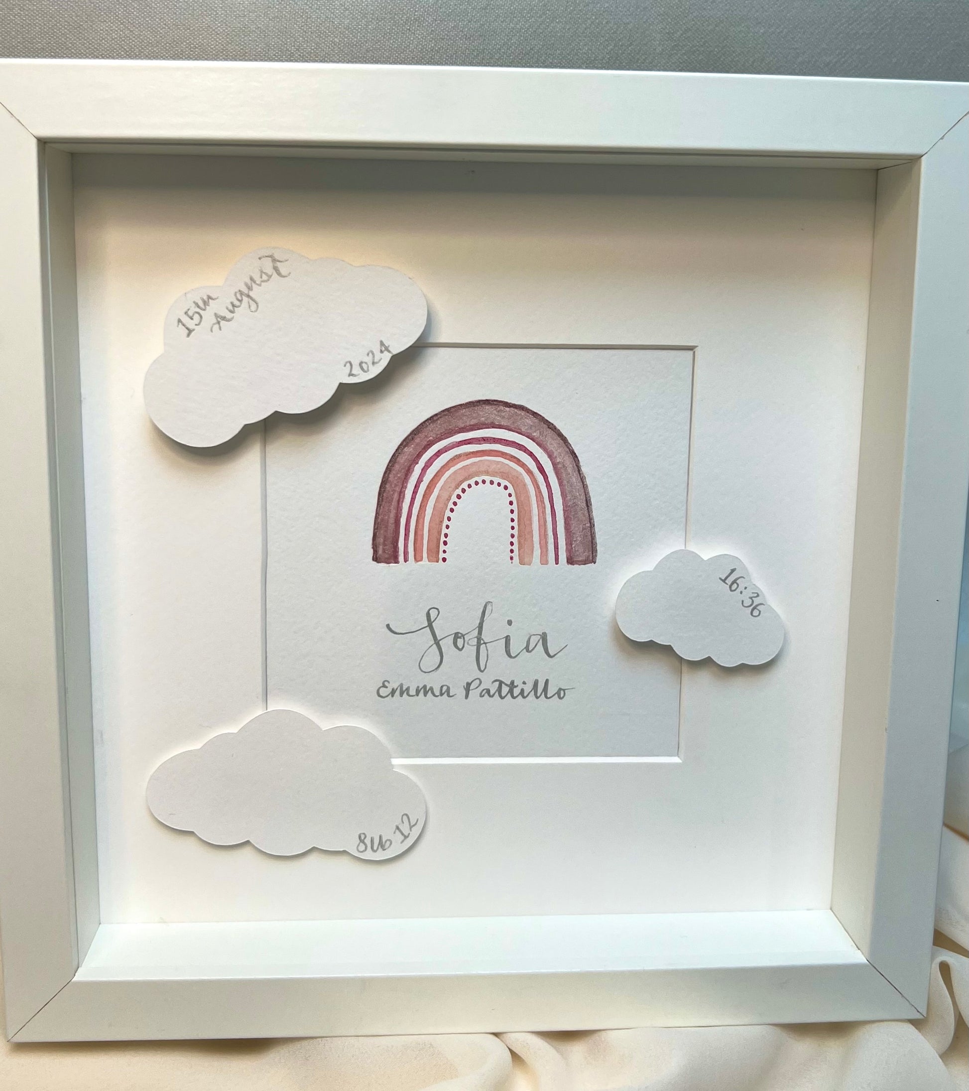 Baby gift - white picture frame with watercolour rainbow in mixed pinks, handwritten baby name in silver ink calligraphy below rainbow with raised clouds around painting detailing baby’s date of birth, weight and time of birth. 