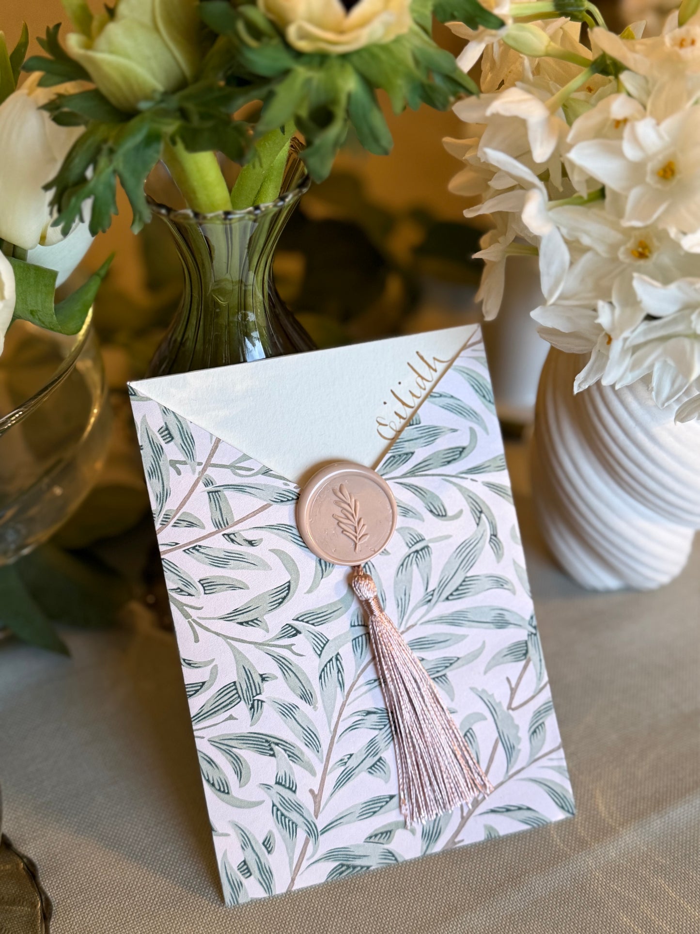 Card with floral design and tassel on a table with flowers in the background