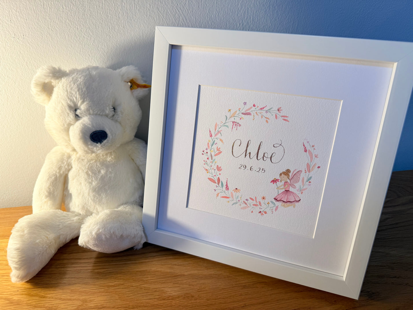 Framed artwork with floral design and teddy bear on a wooden surface