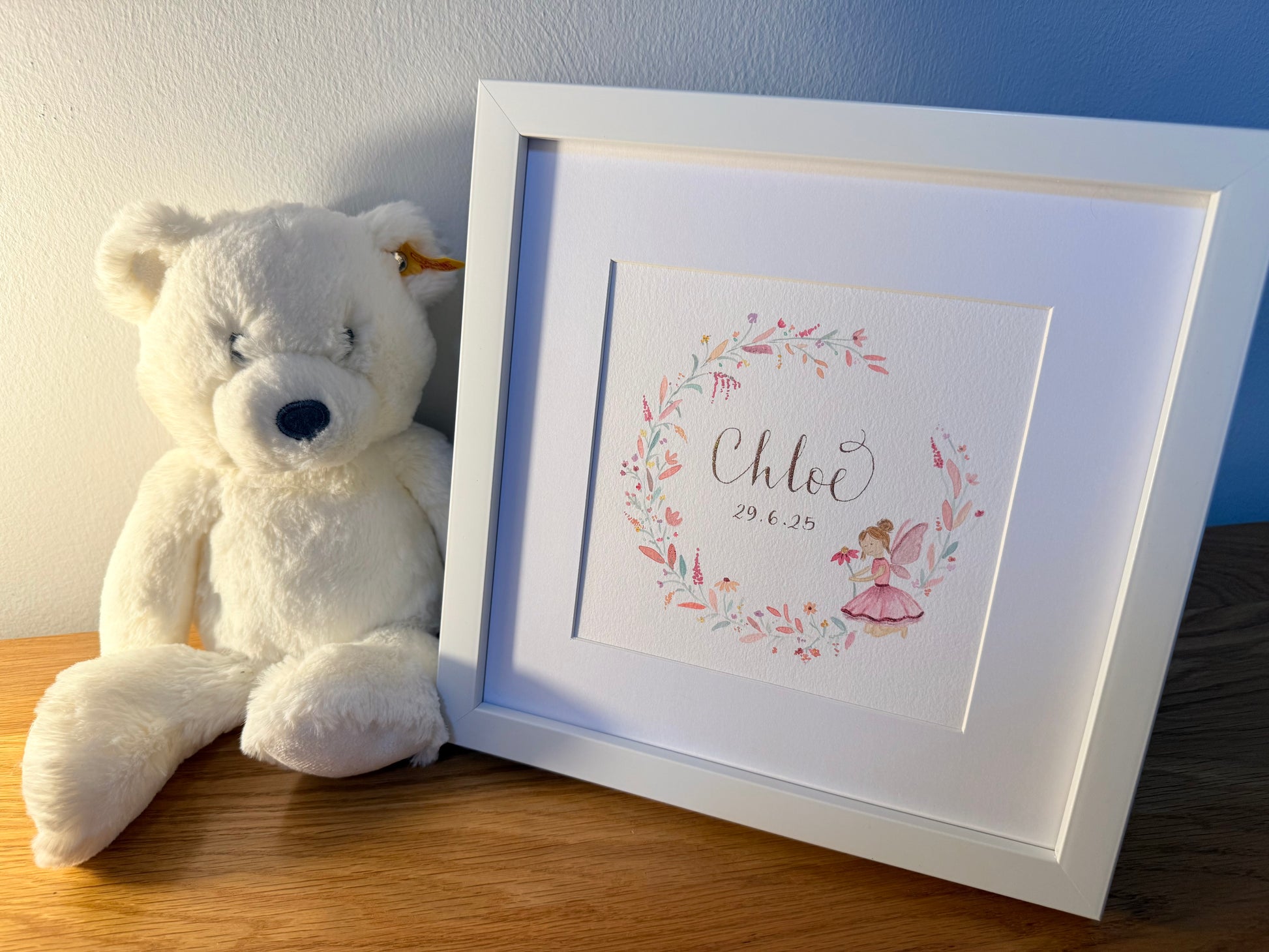 Framed artwork with floral design and teddy bear on a wooden surface