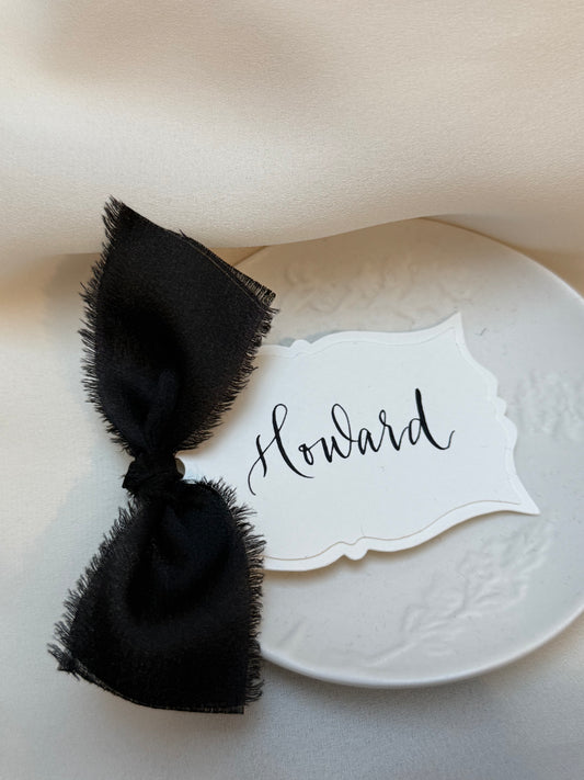 Black bow tie on a white plate with a name card labeled 'Howard' on a beige background