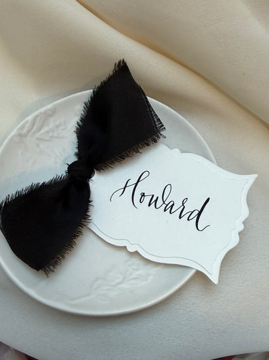 Place card with black bow and 'Howard' text on a white plate.