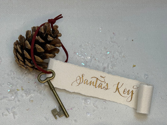Decorative key with 'Santa's Key' tag and pine cone on a textured surface