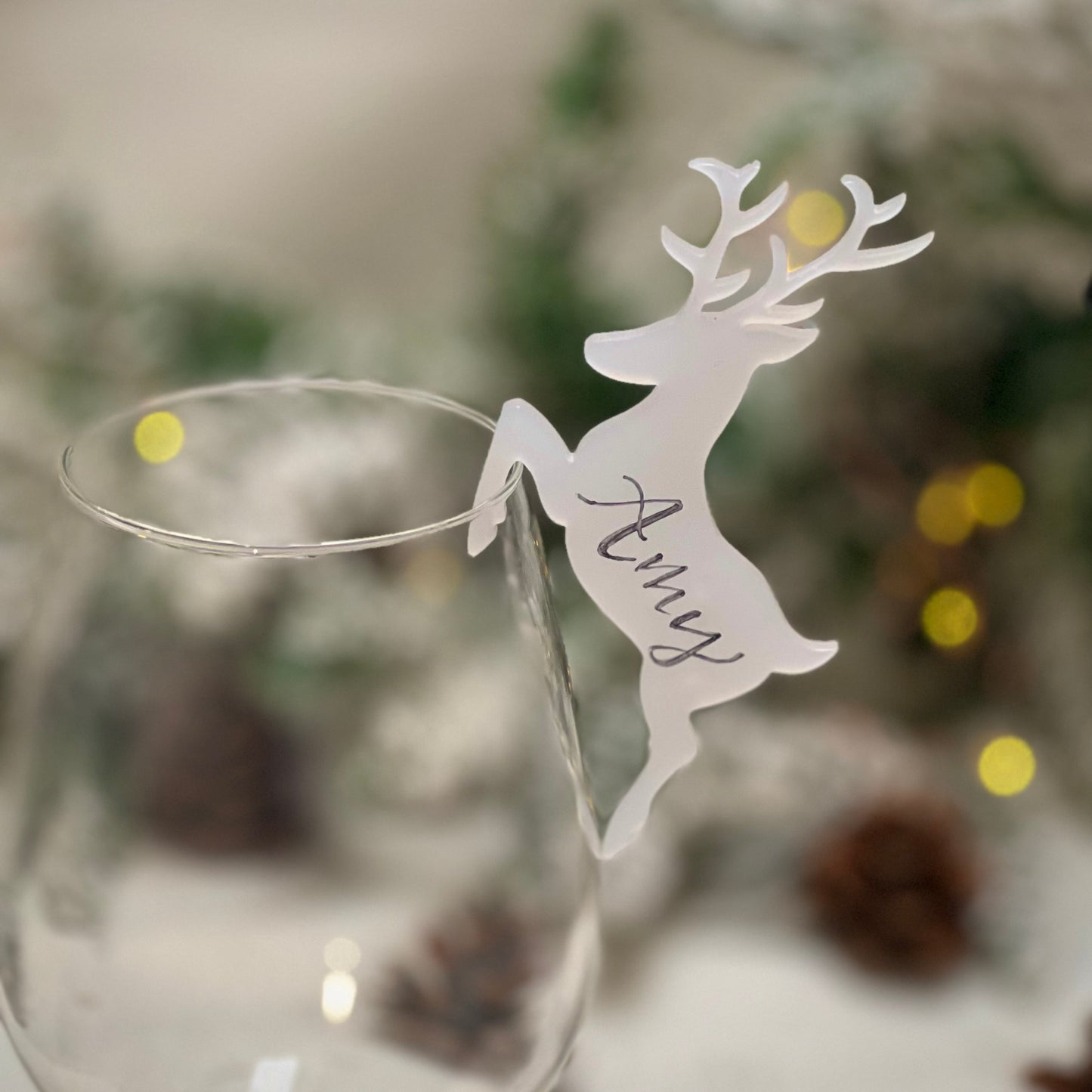 A glass showcasing a nametag in the shape of a detailed deer design, made of flat acrylic. The deer is personalised with the name "Amy" handwritten on the side.