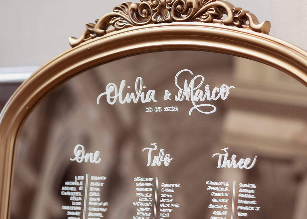Decorative mirror with 'Olivia & Marco' and seating arrangements engraved on it.