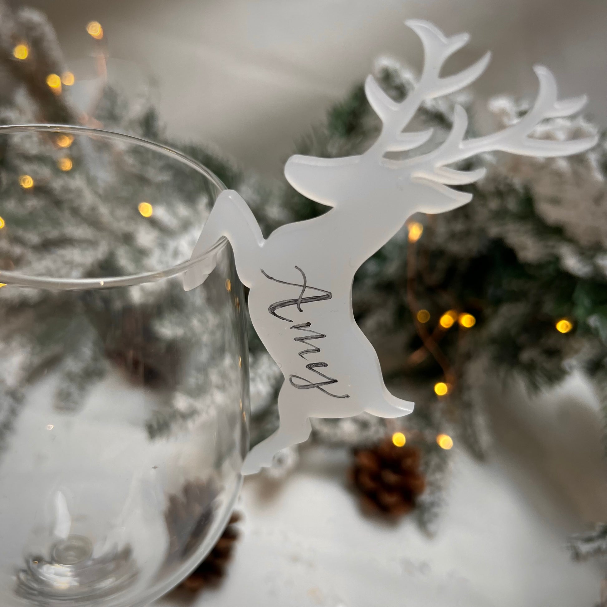 closeup image of a nametag made of frosted acrylic in the shape of a deer resting on the side of a wine glass. The deer is personalised with the name "Amy" handwritten on the side in calligraphy.