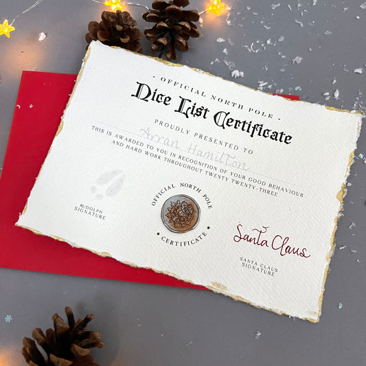 A bespoke Nice List certificate from the North Pole awarded to a child, signed by Santa Claus and Rudolph, placed on a red envelope with pinecones and festive lights in the background. the card has golden, frayed edges and is hand written.