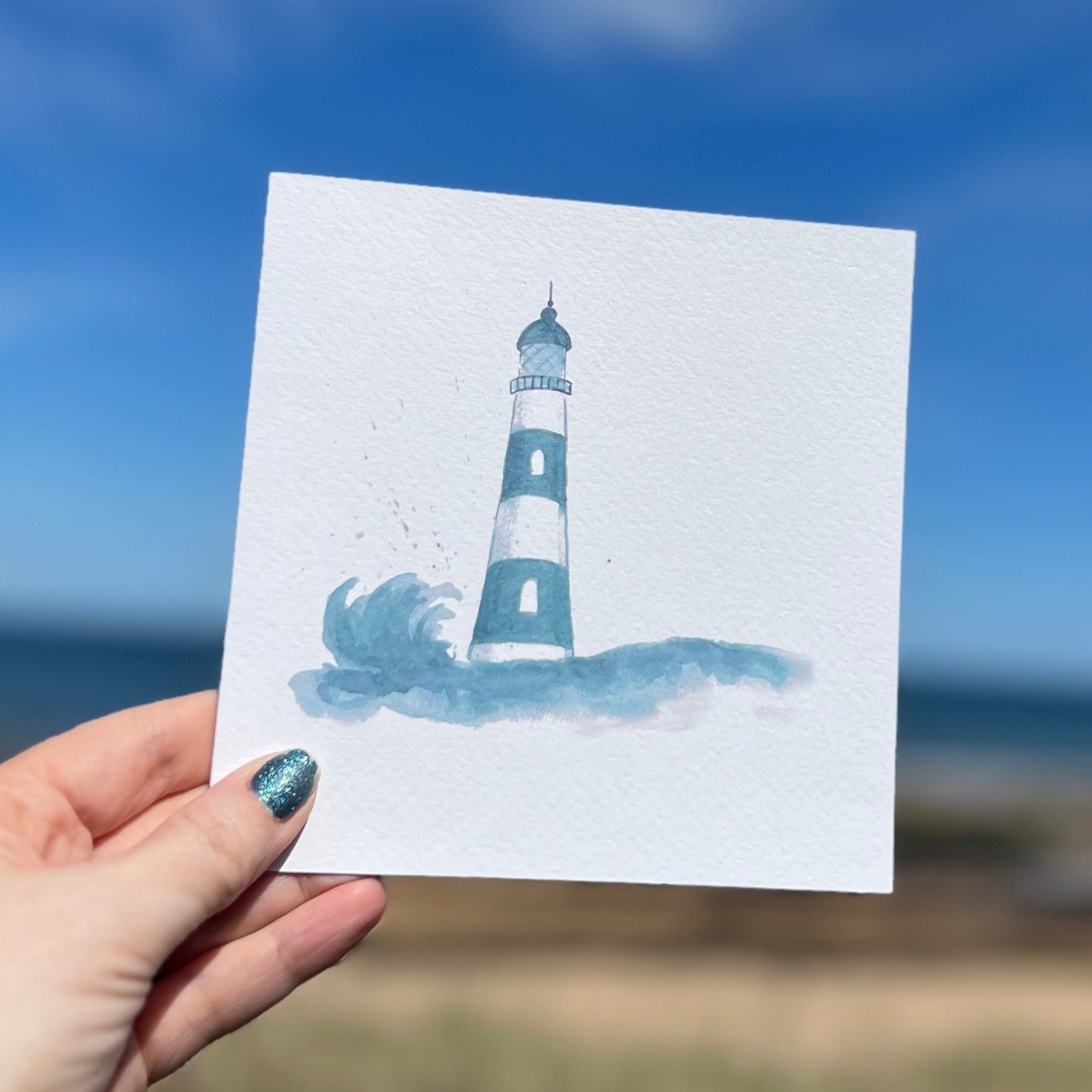 Watercolour greetings card of blue and white lighthouse with wave and splashes