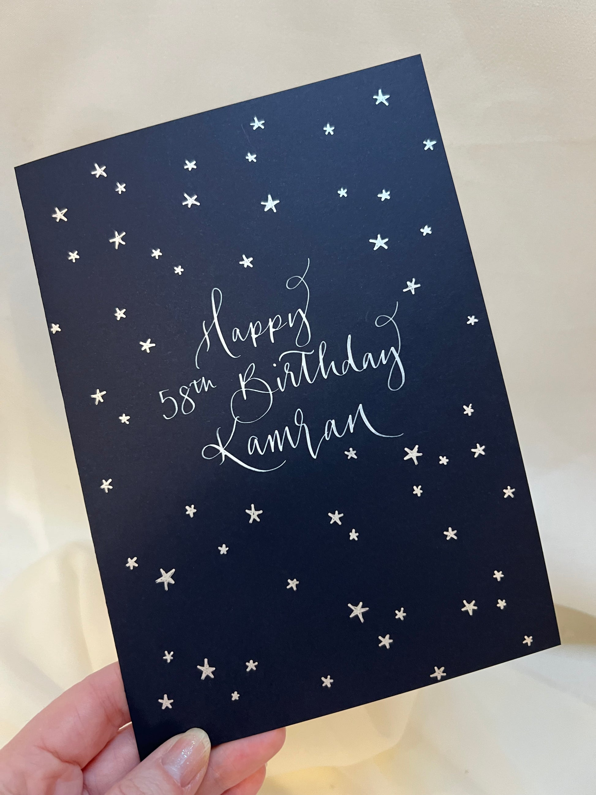 Navy card with calligraphy wording ‘happy 58th birthday Kamran’. Surrounded by 58 hand drawn silver stars 