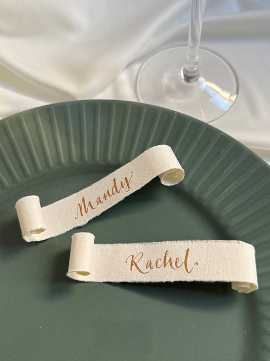 Two cotton paper scroll name tags on a green plate with a glass of wine in the background