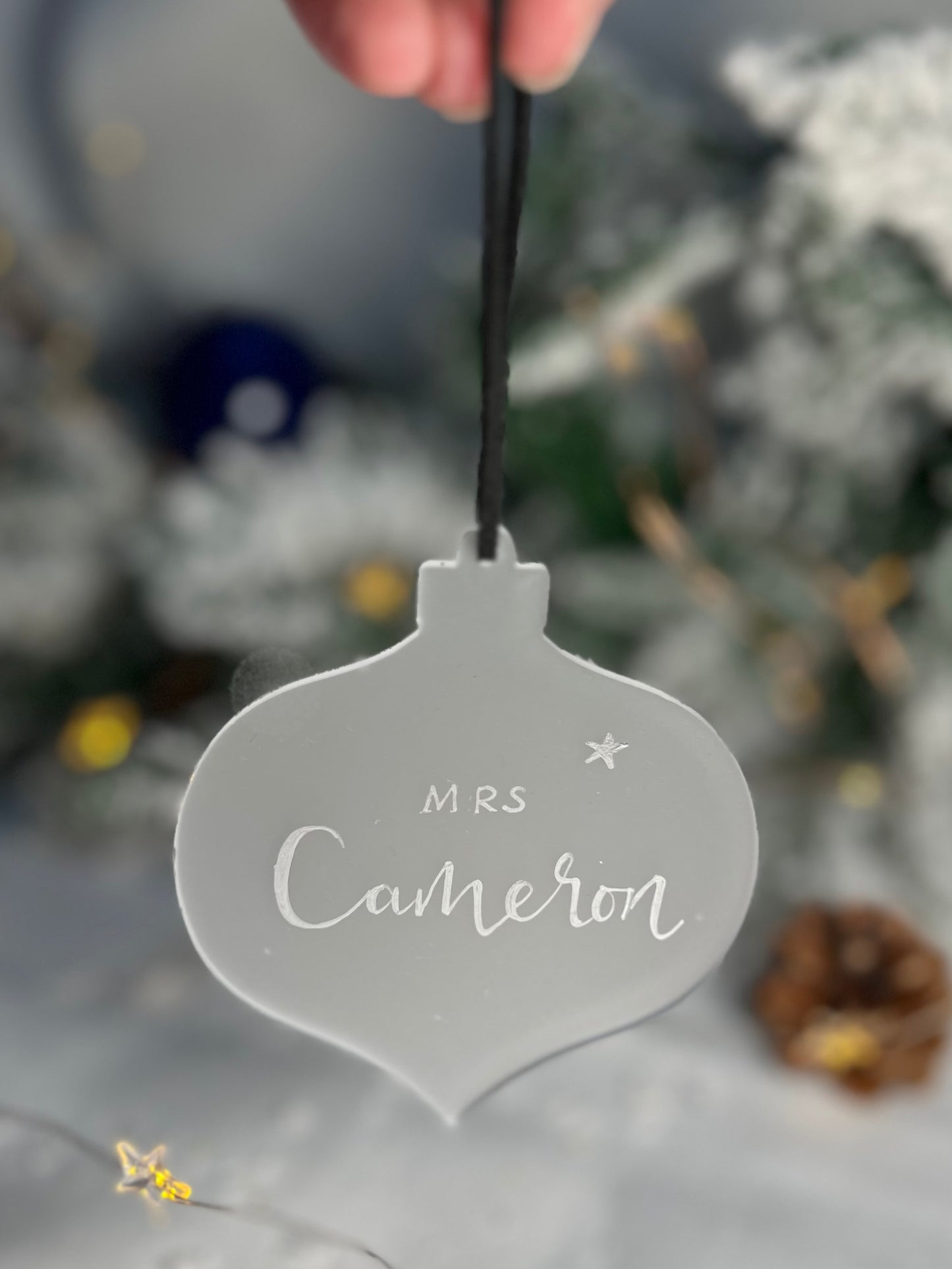 Hanging flat Perspex Christmas bauble with Mrs Cameron handwritten in silver ink. Hanging with black ribbon