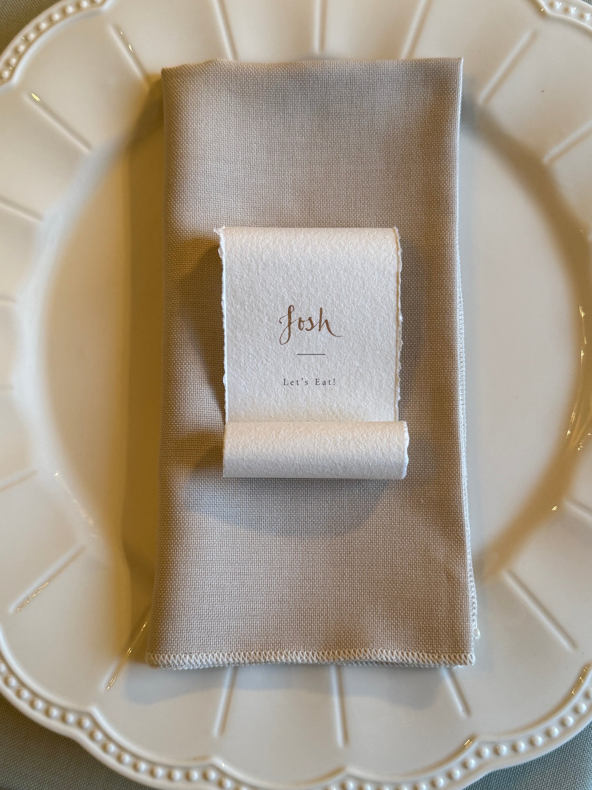 Folded beige napkin with a scroll menu name card on a white plate