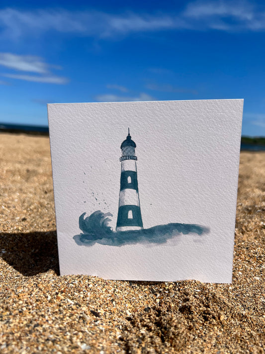 blue and white lighthouse card sitting on sand with beautiful blue sky