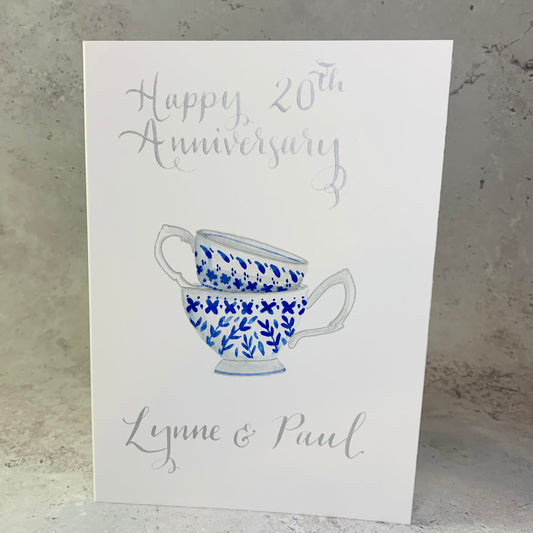 A bespoke card featuring a delicate blue and white teacup, elegantly adorned with handwritten calligraphy and cantered on a soft marble background.