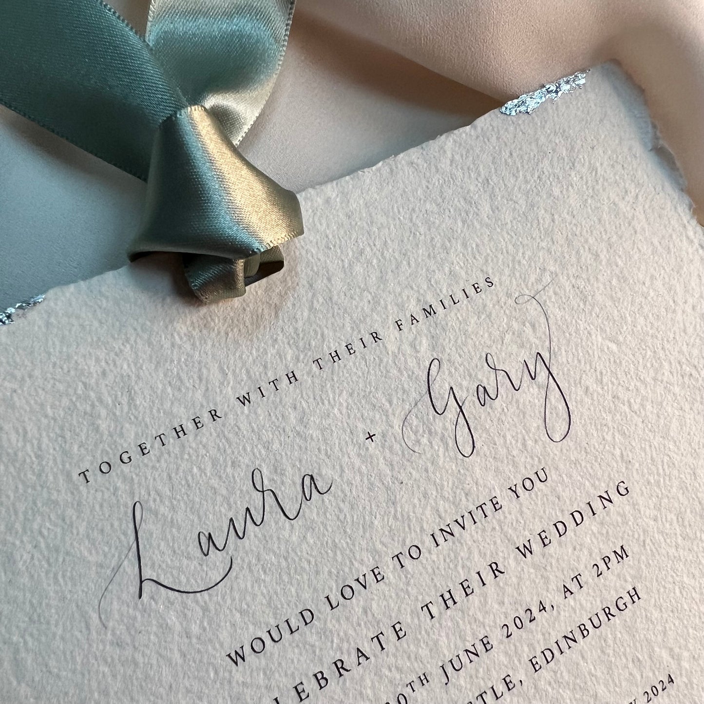 Close up of wedding invitation soft edged handmade paper, green satin ribbon, silver leaf  around edges