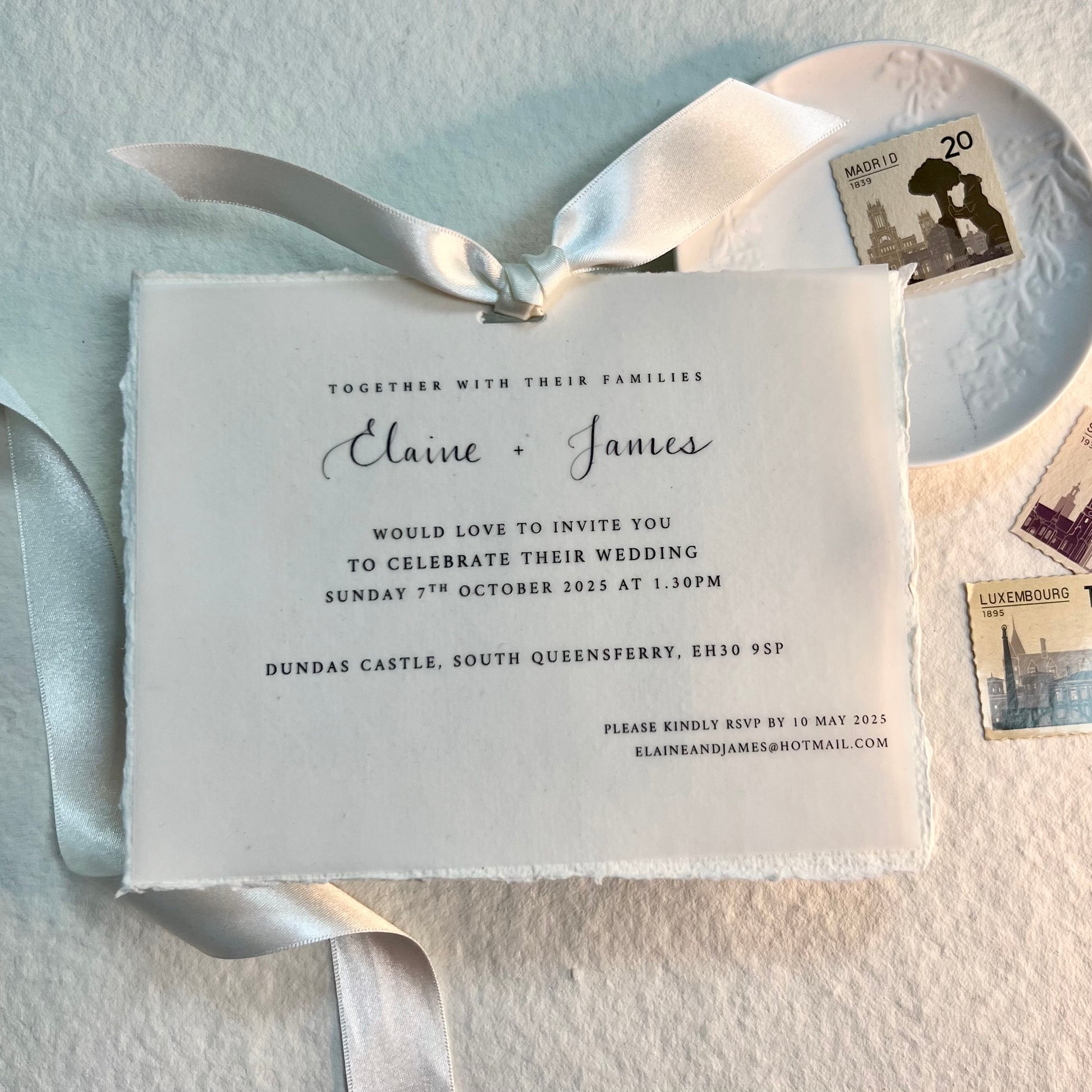 handmade paper with vellum invitation tied with ivory satin ribbon. styled in picture with trinket dish and stamps with draped ribbons