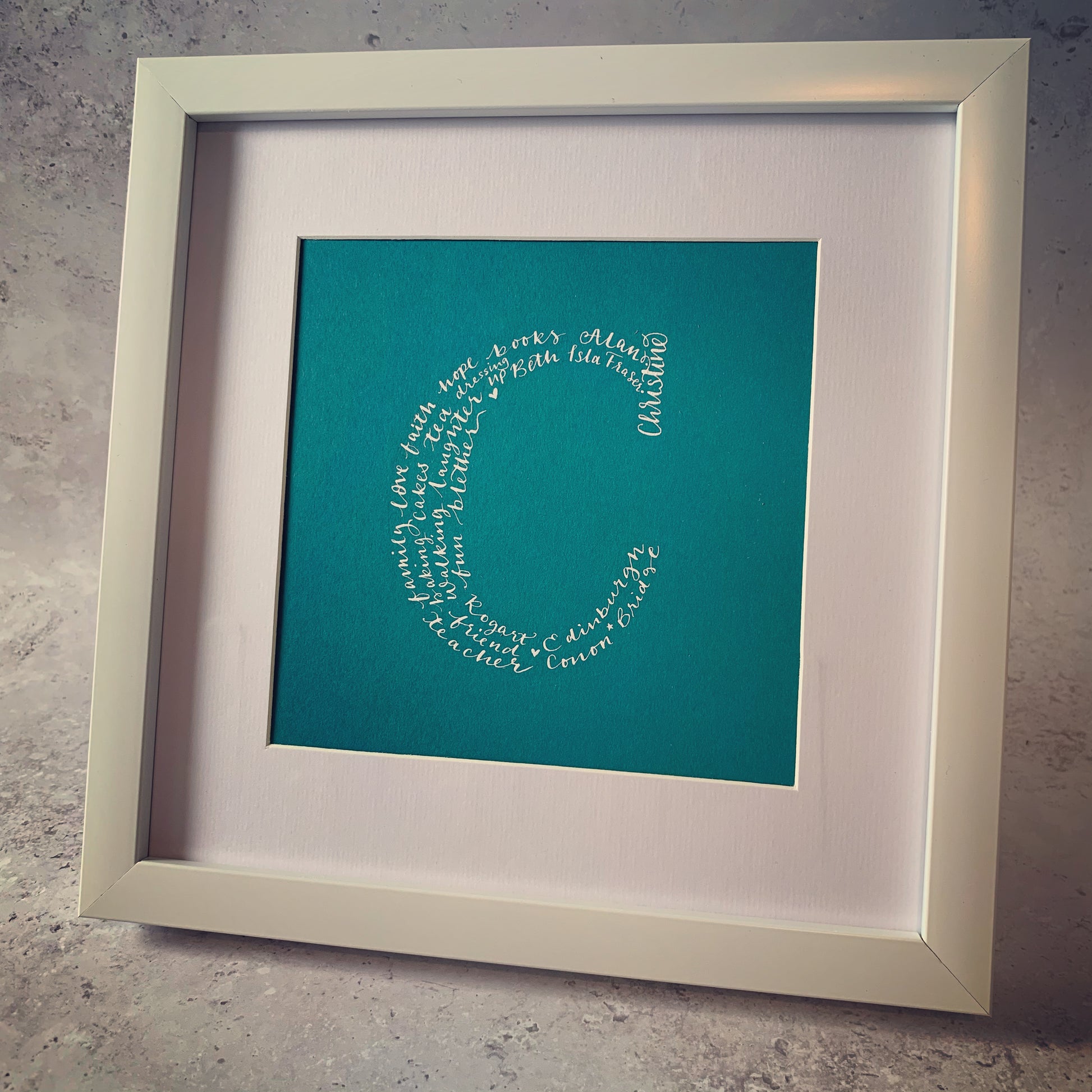 A custom shape calligraphy artwork in a teal color, framed in a white square frame, with a visible text pattern within the shape of the letter 'C'.