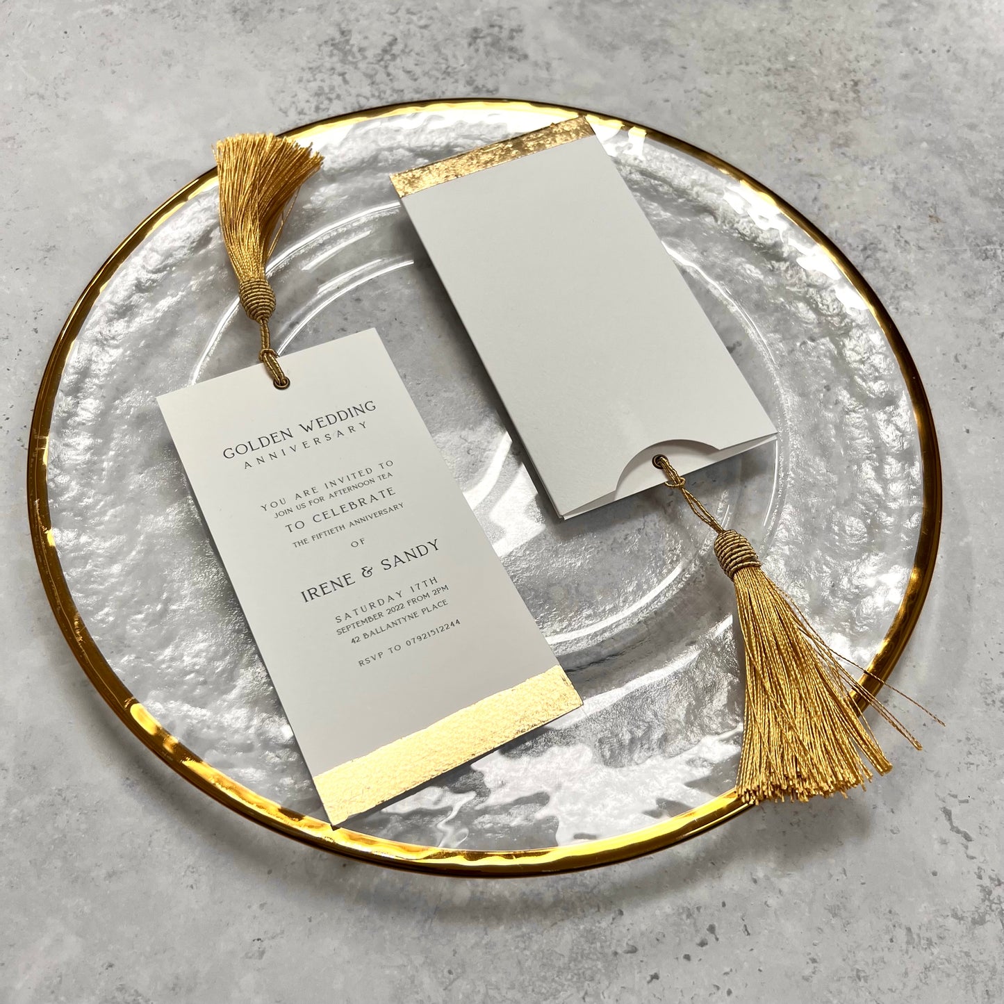invite with gold tassel and wallet gold foil line at bottom. on gold charger plate 