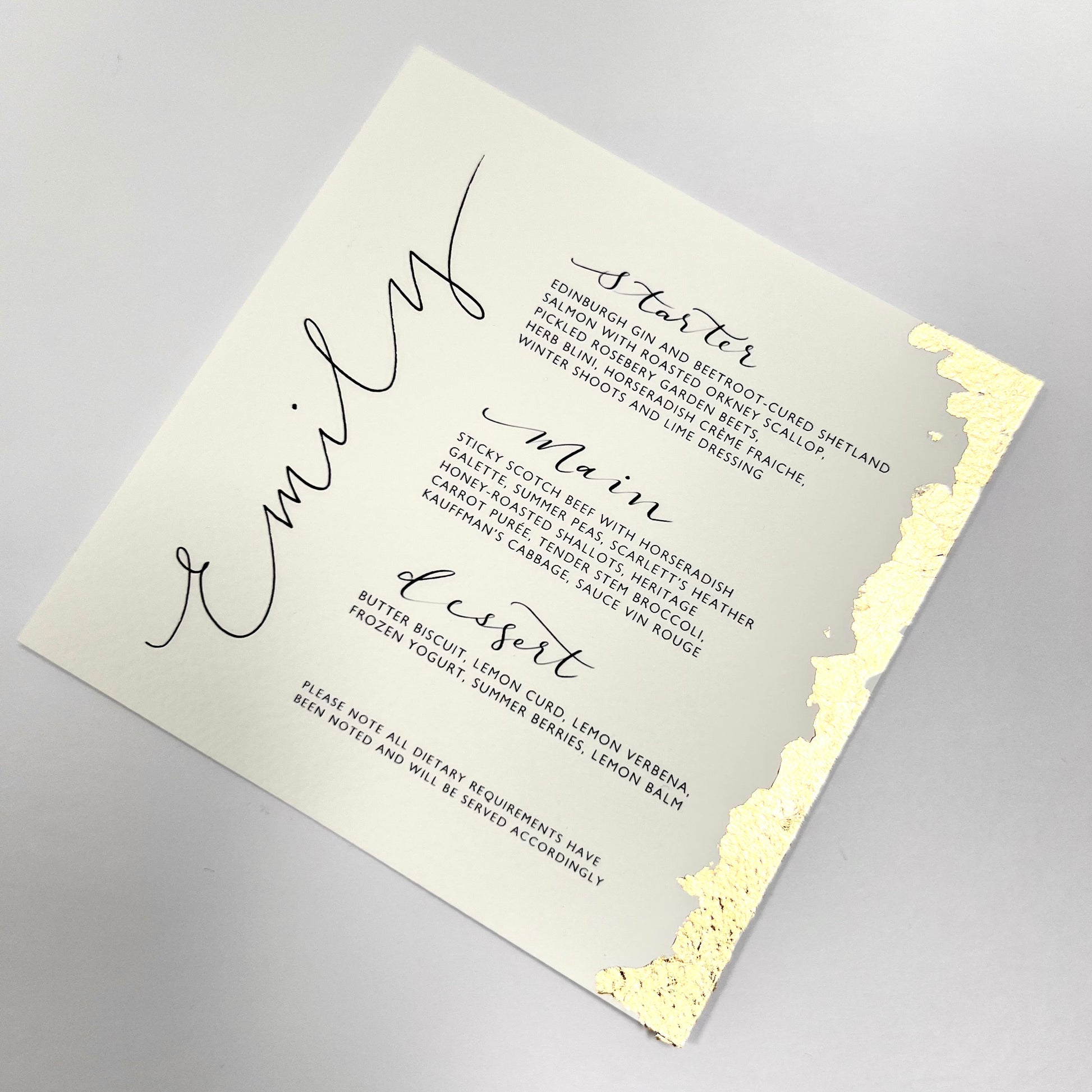 A menu card with guest name elegantly hand written in calligraphy , gold leafed on the right side of the menus and a flat white background.