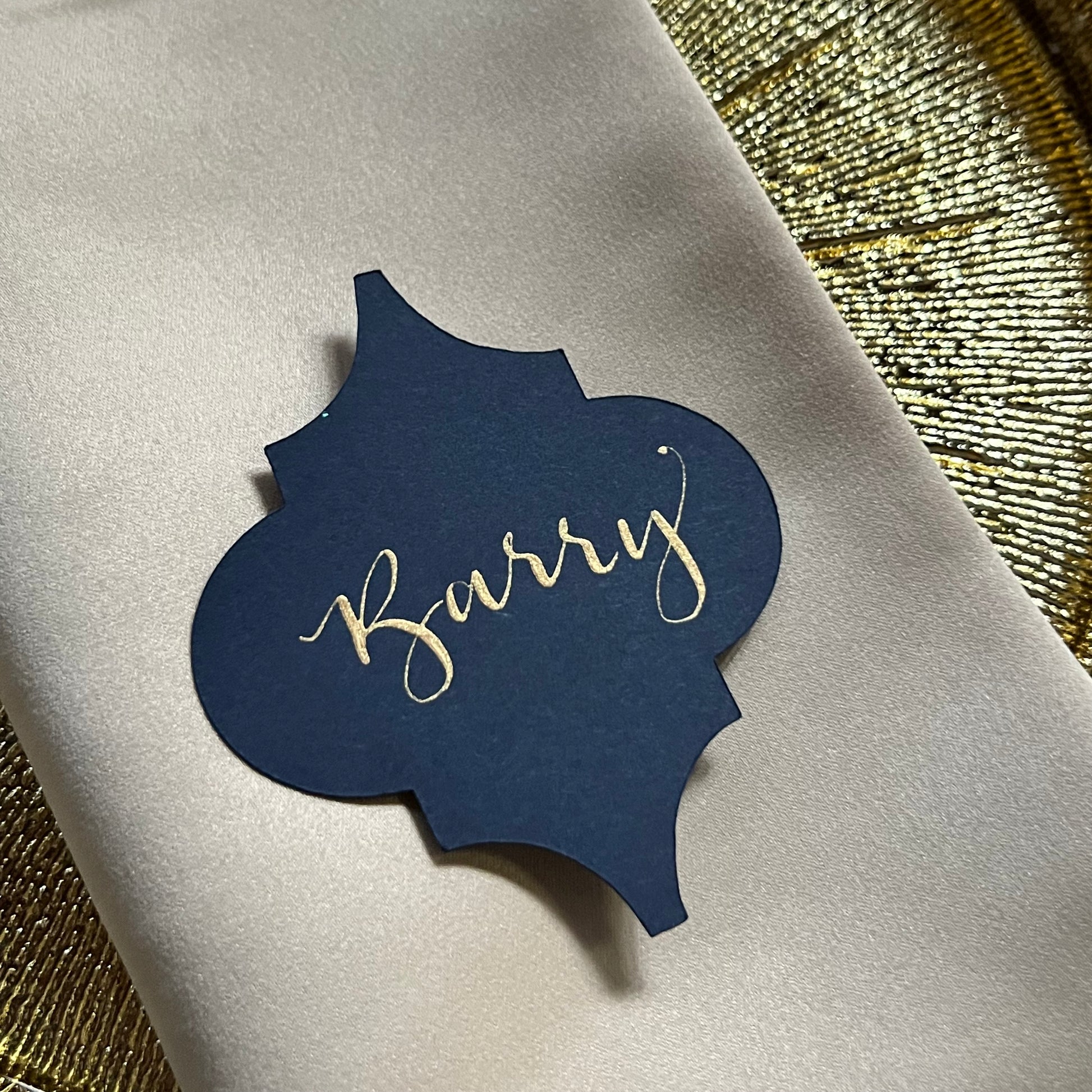 close up of navy card in shape of moroccan tile, with shimmering gold ink calligraphy name Barry