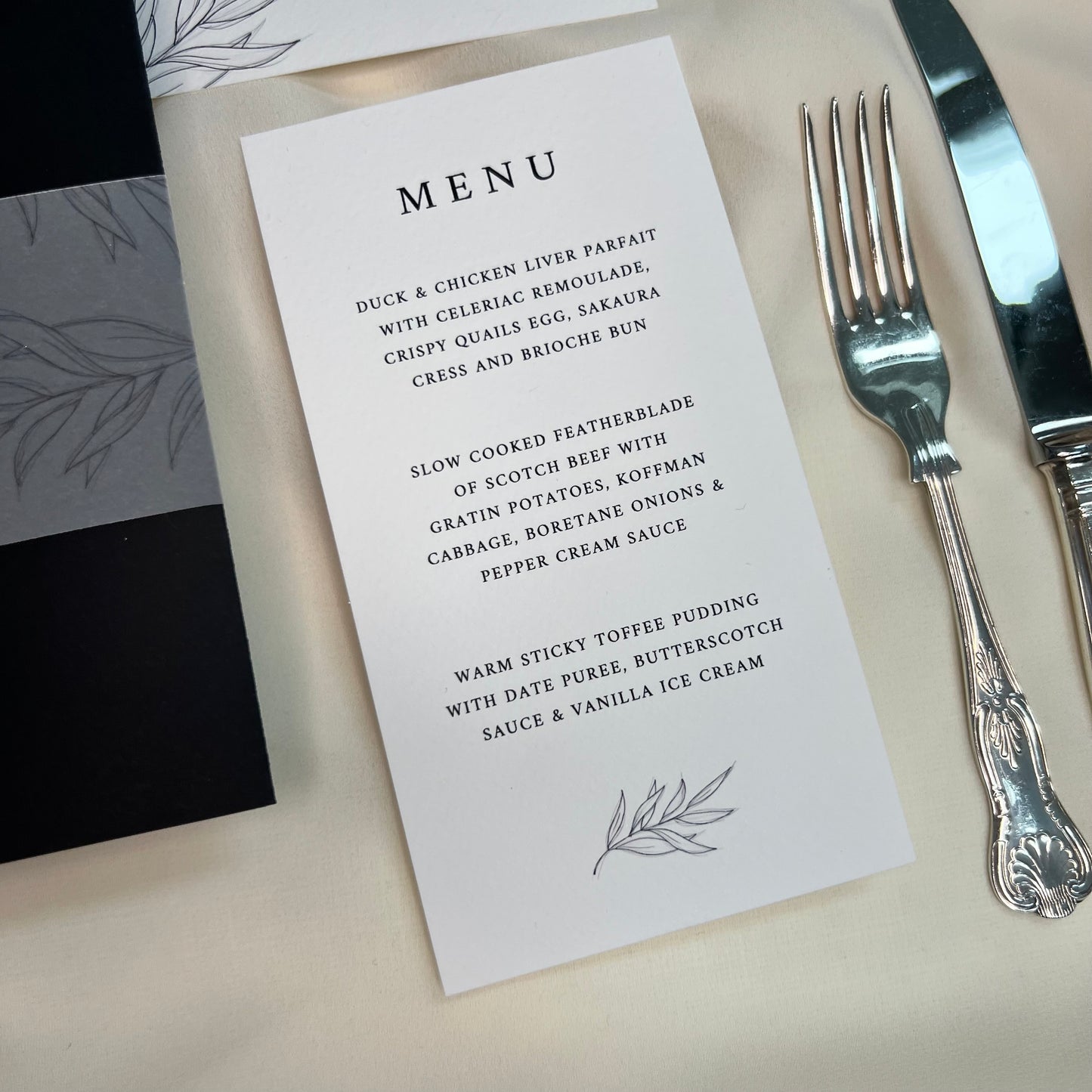 black and white menu with foliage sketch. other stationery and beautiful cutlery to side
