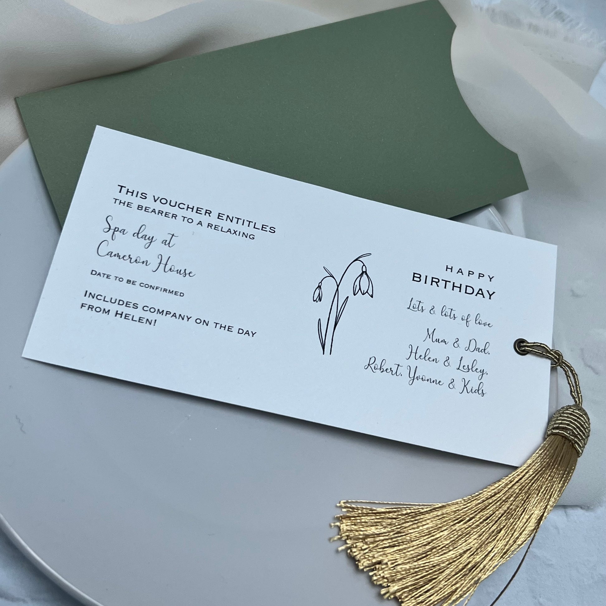 green wallet with white textured card gift voucher finished with gold tassel and snowdrop drawing 