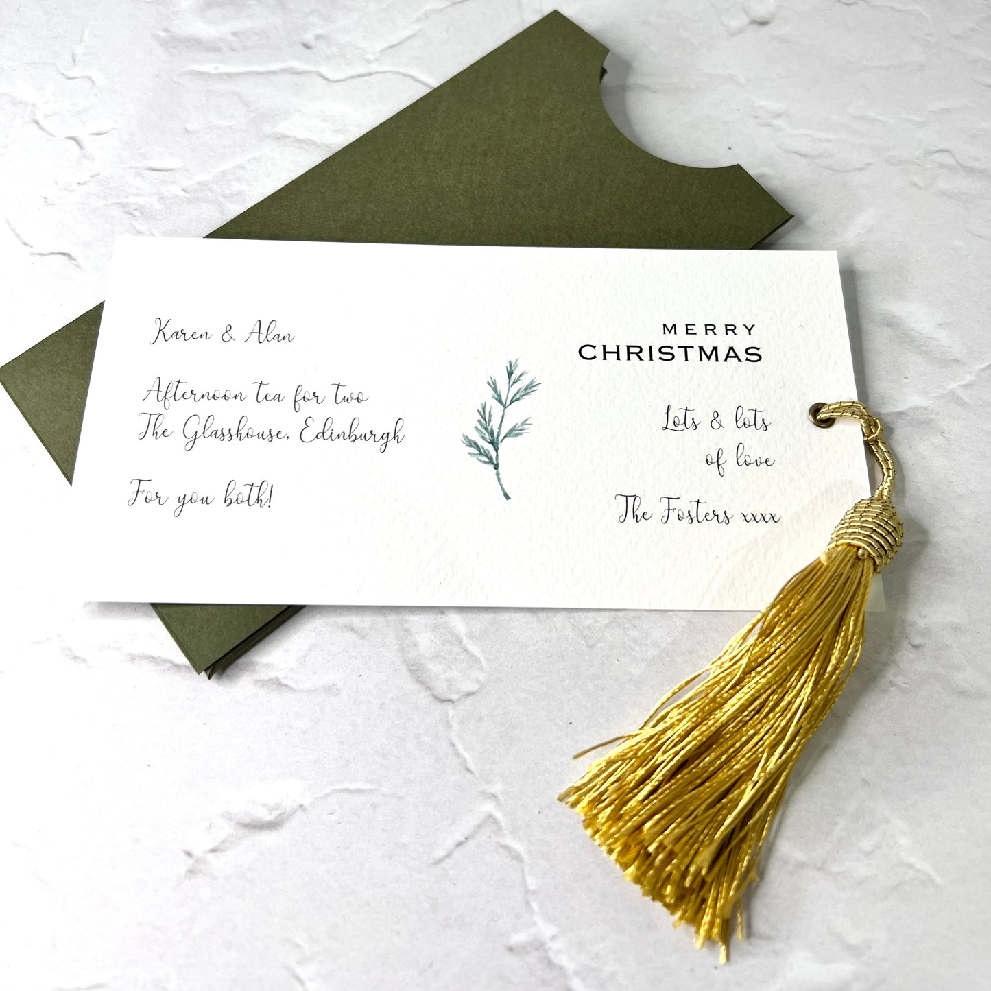 gift voucher on white card with gold tassel and sprig of pine, in moss green wallet