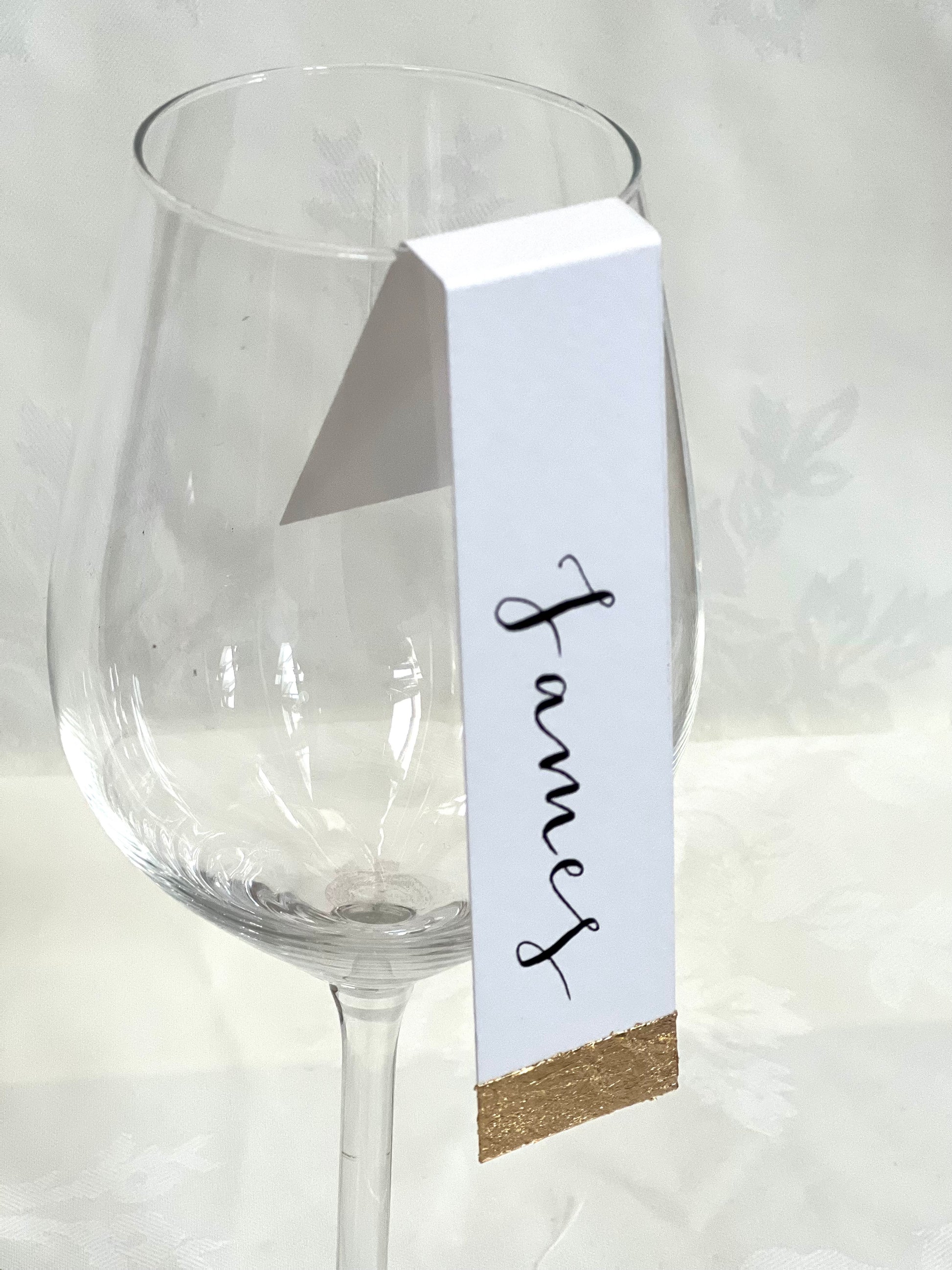 wine glass tag with gold foil detail at bottom and guest name written down the way off wine glass 