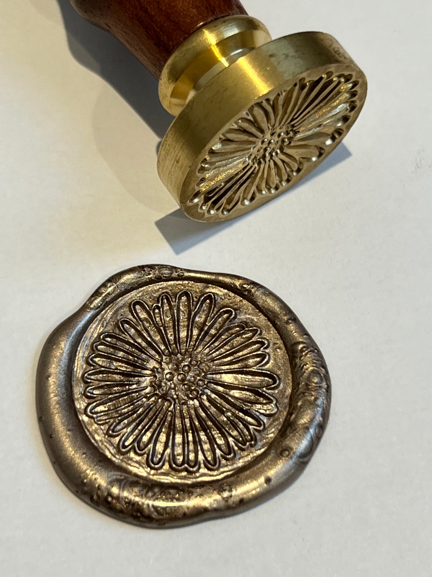 daisy wax seal stamp with gold wax seal lying beside it with the same daisy design