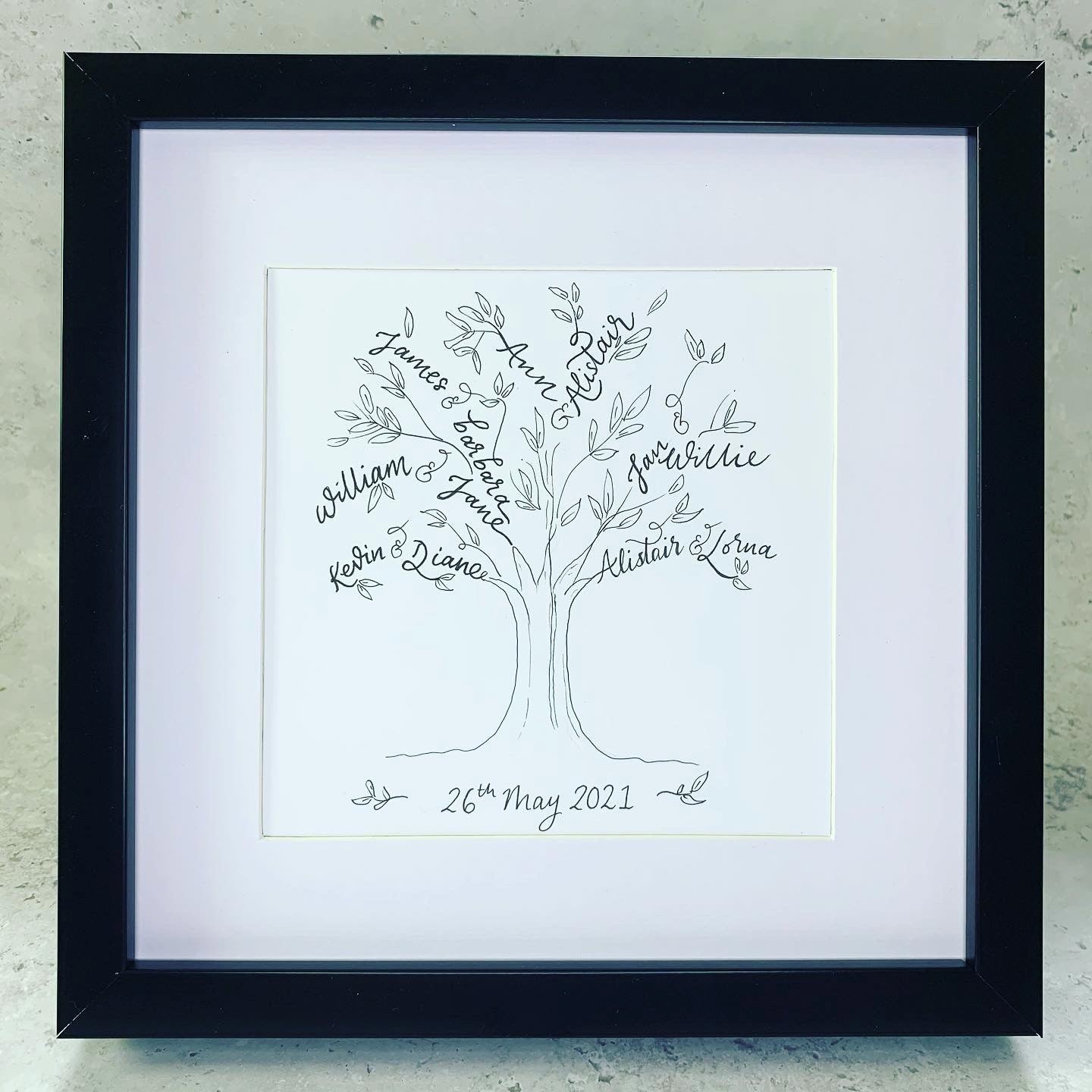 black picture frame with hand drawn family tree within mount, all black and white. 