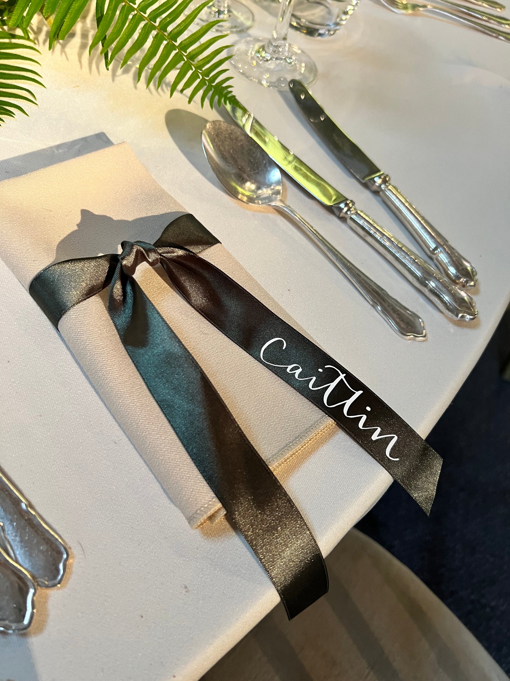 Personalised green ribbon with white name, tied around napkin from 88 events, on beautifully set table with ferns 