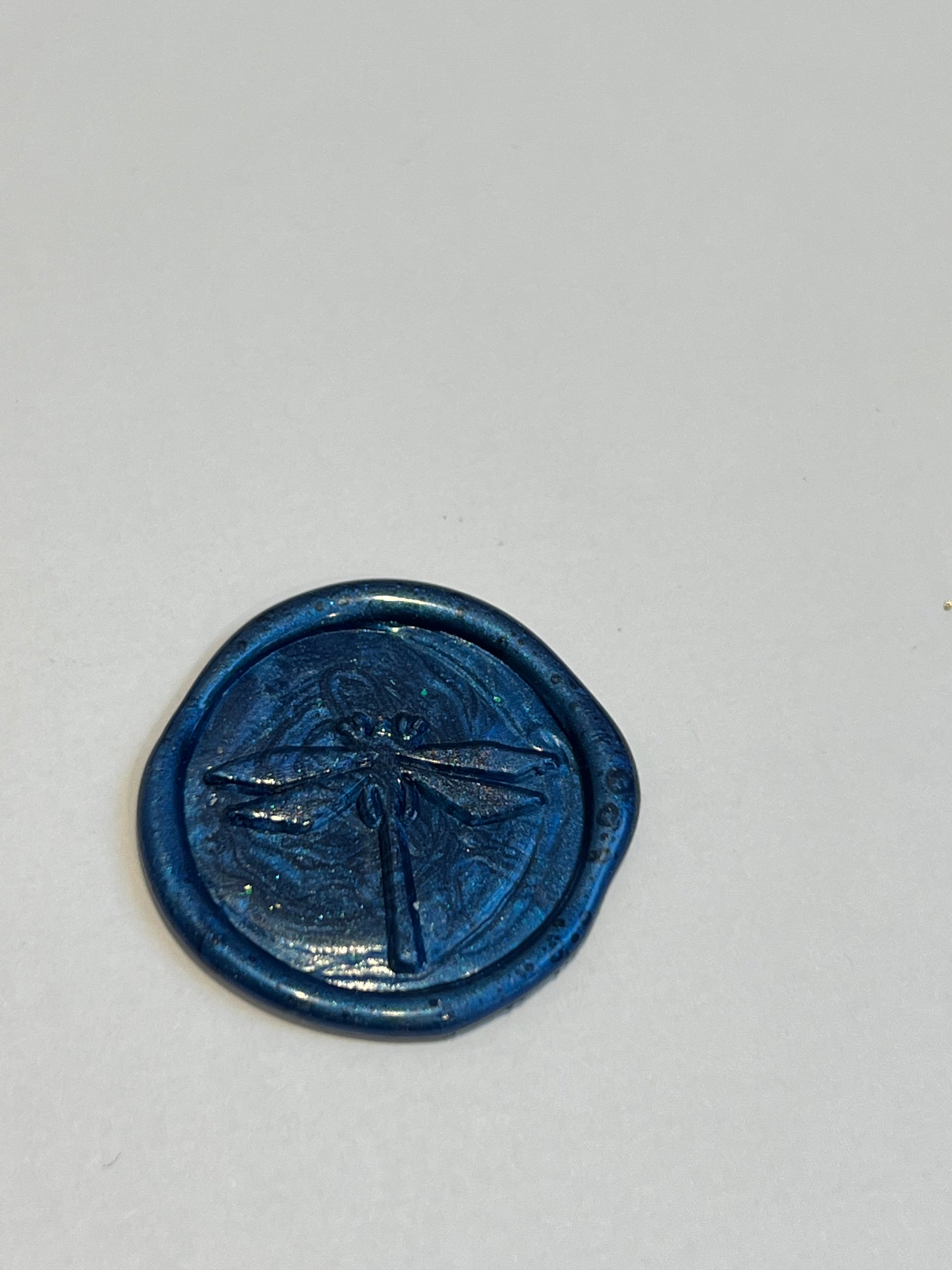 navy blue wax seal with glitter through it in a dragonfly design