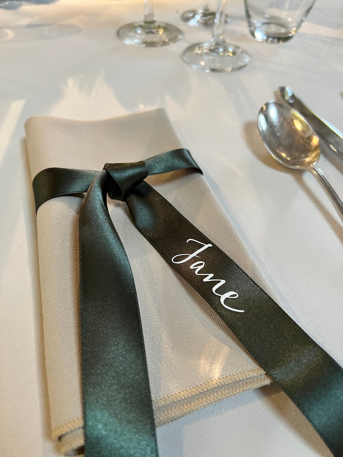 biscuit coloured napkin with green ribbon tied around, guest name on napkin - Jane