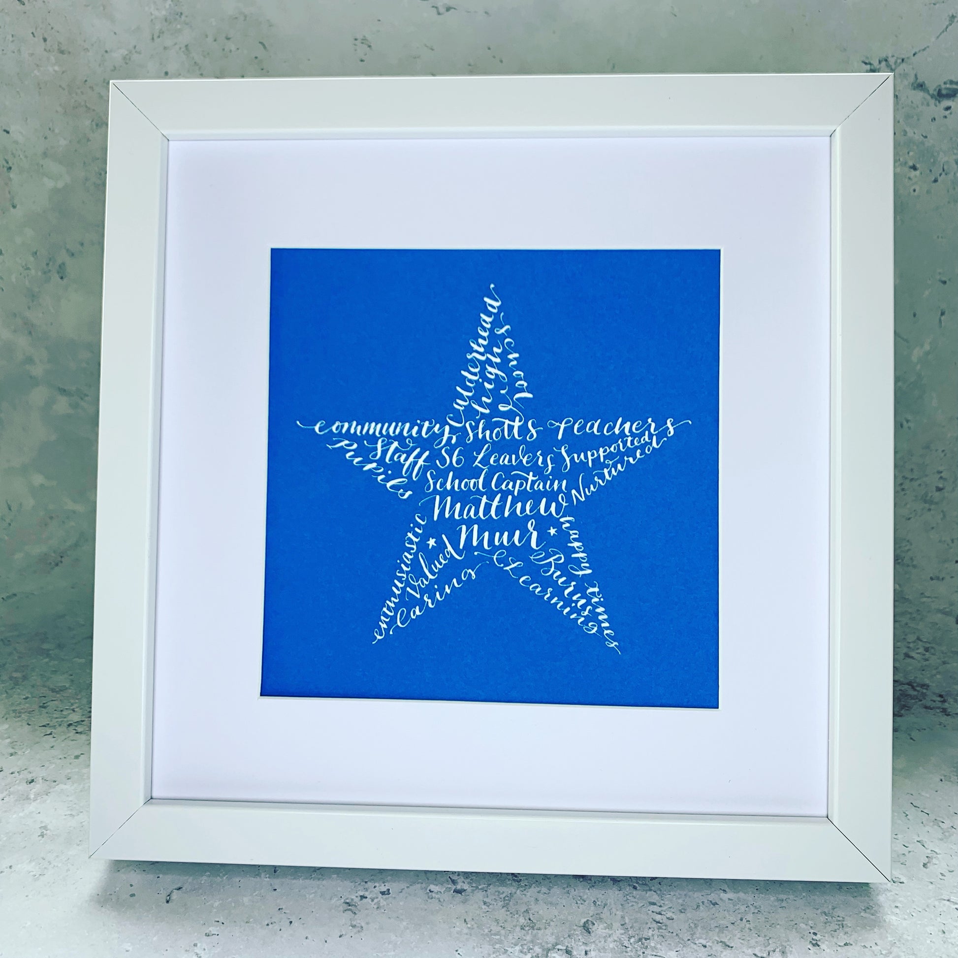 white square picture frame with white mount filled with blue card. white ink calligraphy making up star shape