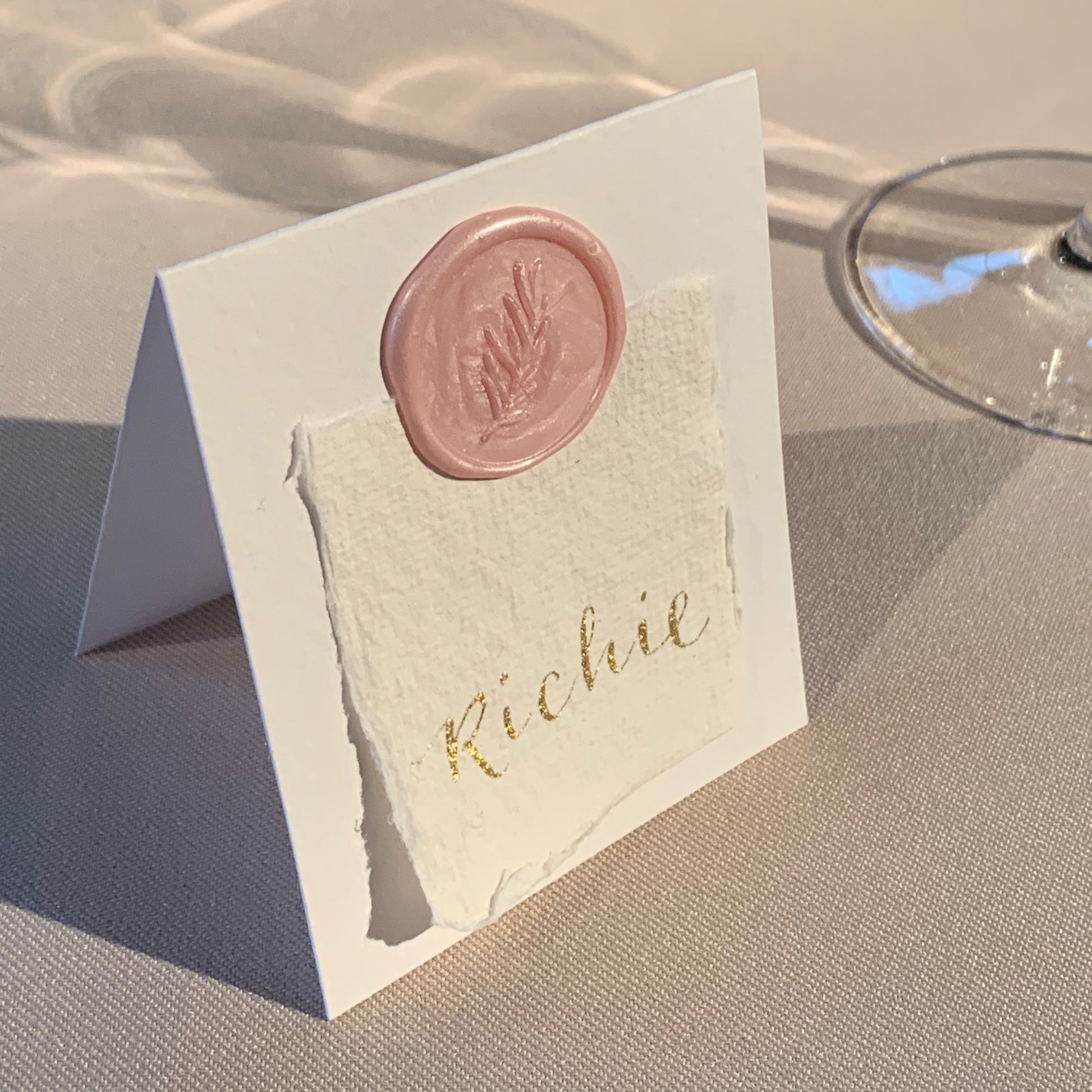 elegant place card, guest name written on cotton paper in gold ink, attached to place card with pink wax seal