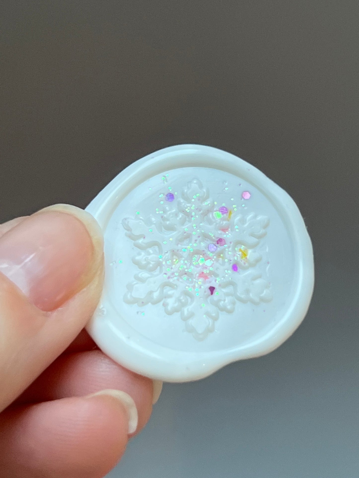 close in picture of a hand holding a white wax seal with a snowflake design and glitter.