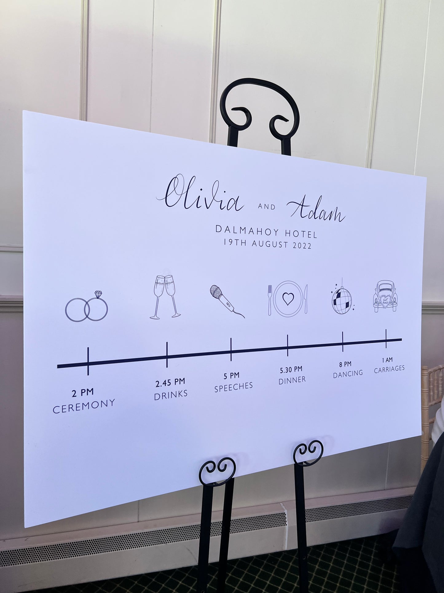 sign on black easel, doodles for each timing. order of day sign. ceremony rings, drinks glasses, speeches mic, dinner plate with heart, dancing glitter ball, carriages just married car