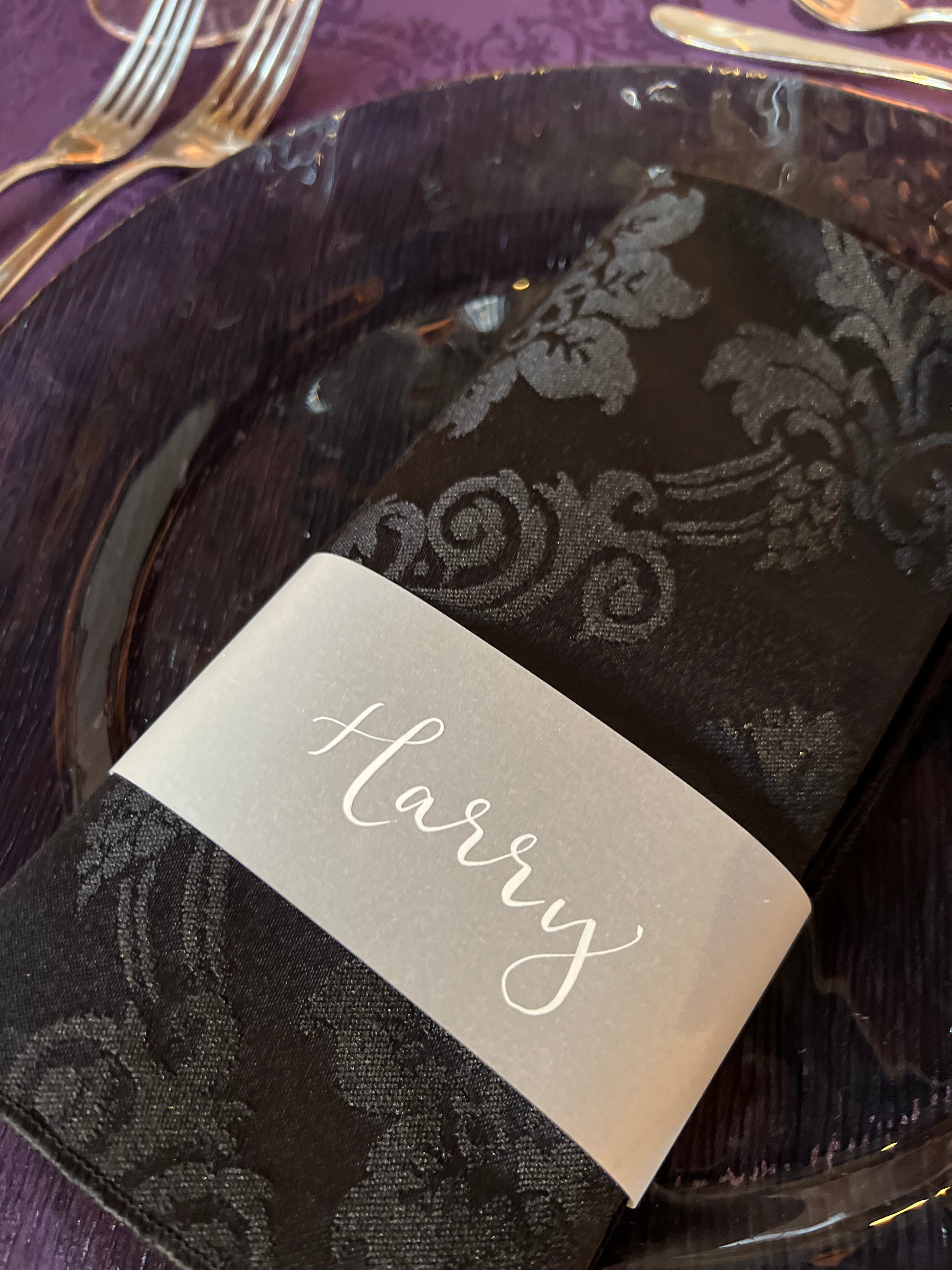 Black napkin on black charger plate with plum damask cloth, napkin finished with vellum cuff guest name 