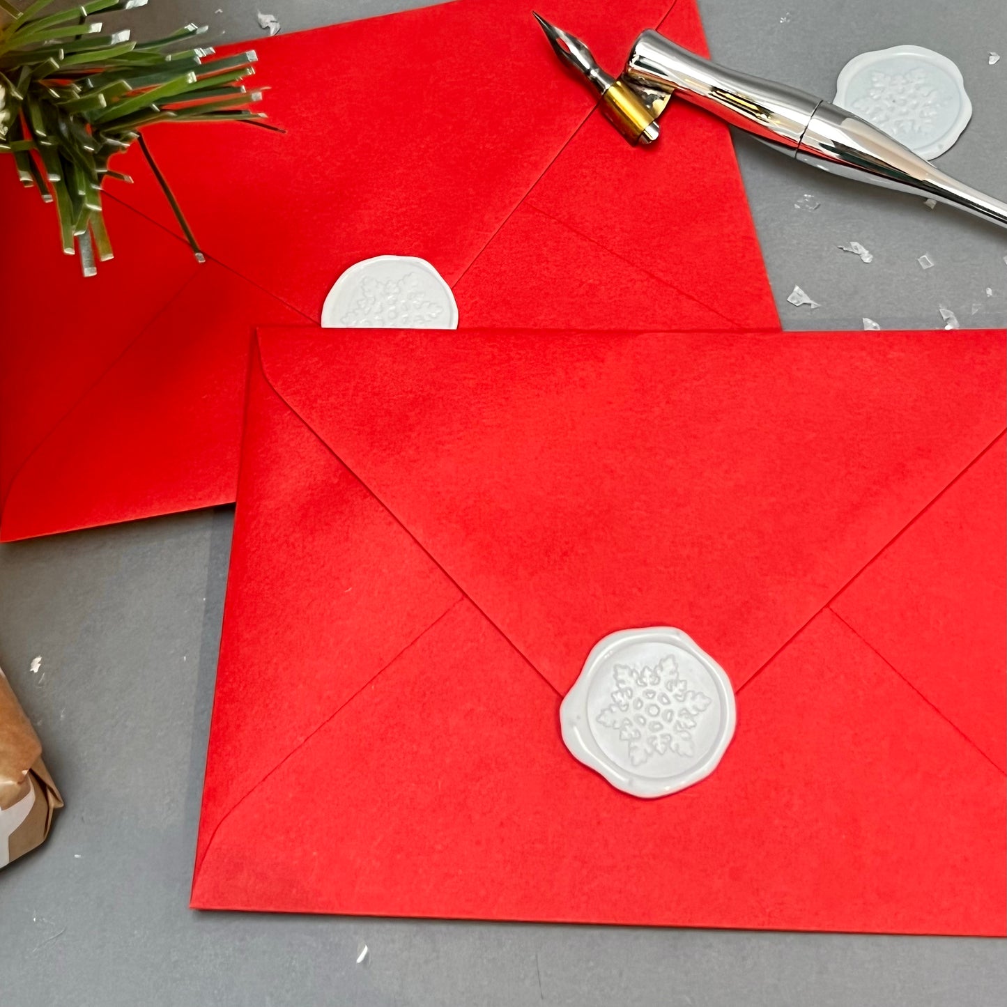 Handmade snowflake wax seals closing two red envelopes which are overlapping each other. calligraphy pen and snowflakes to the side