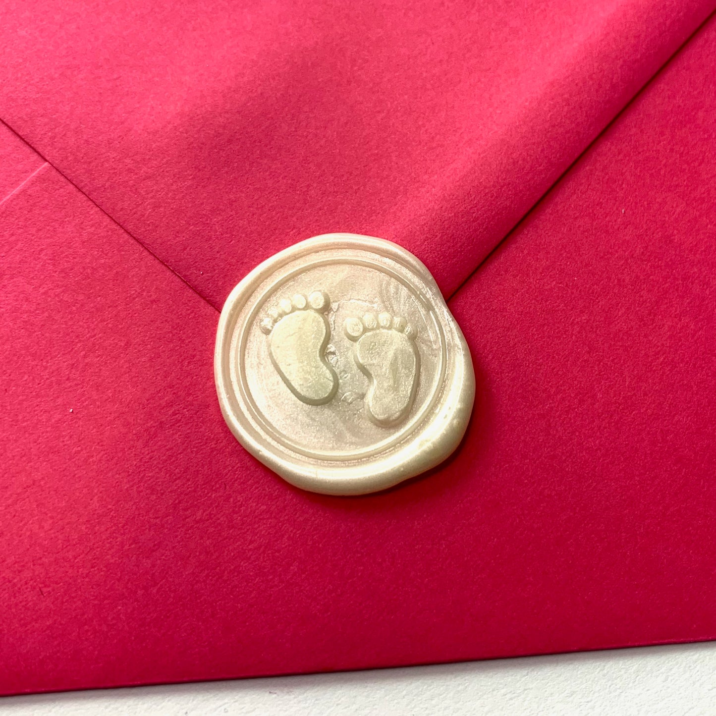 white wax seal on bright pink envelope wax has baby toes and feet design
